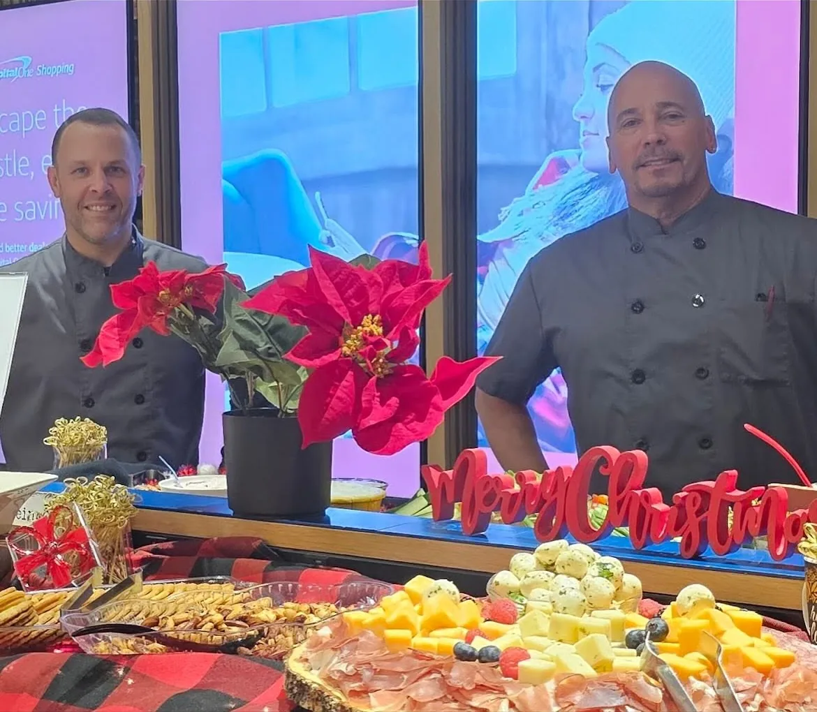 The two owners of Global Fusion RVA behind a catering display of charcuterie and cheese at a corporate holiday event