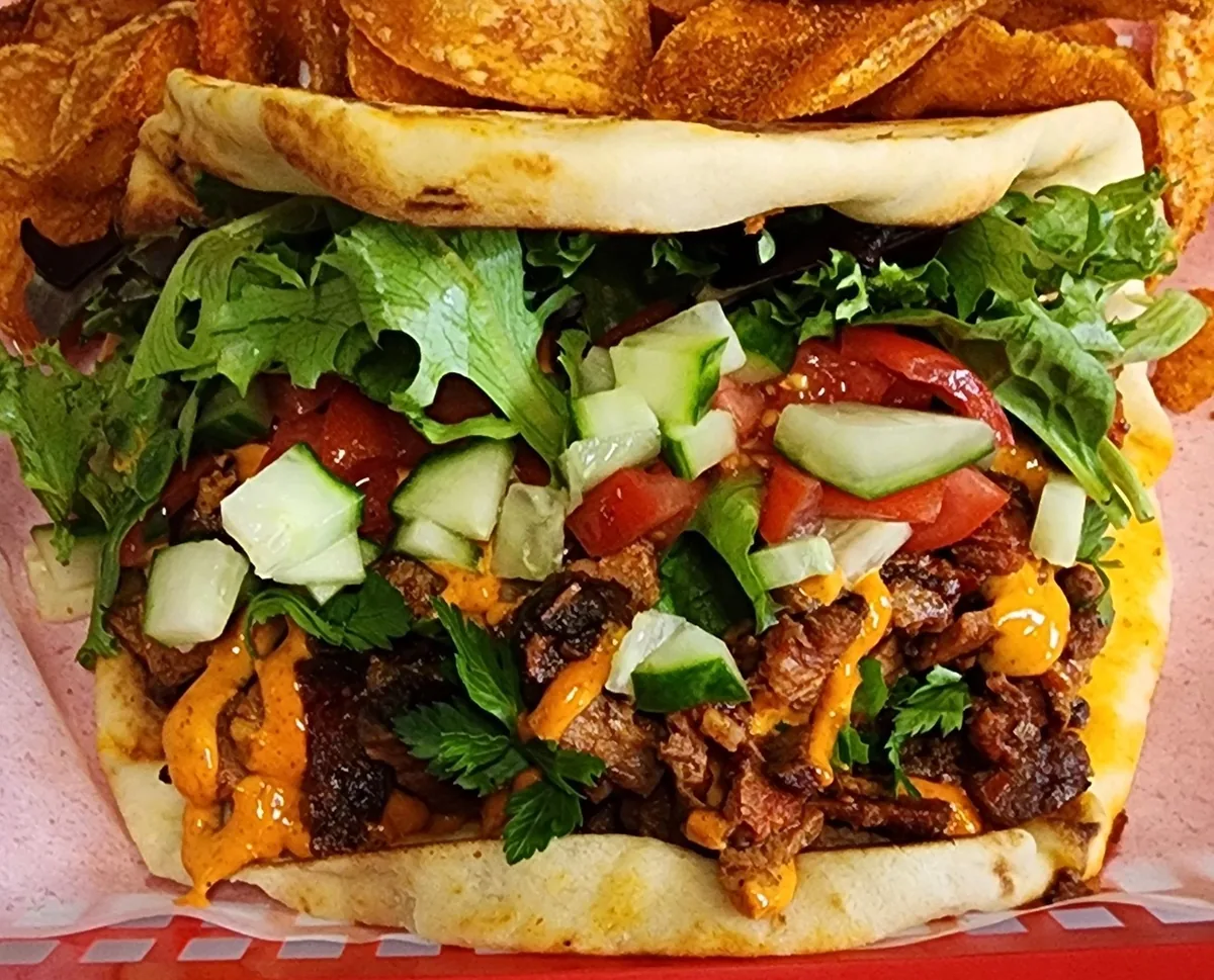 Casablanca sandwich on grilled pita, shown whole with grilled meat, fresh tomato, cucumber, and greens