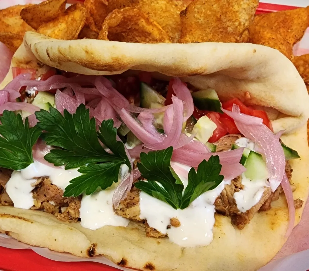 Pulled meat sandwich with tzatziki, pickled red onion, and parsley on grilled pita