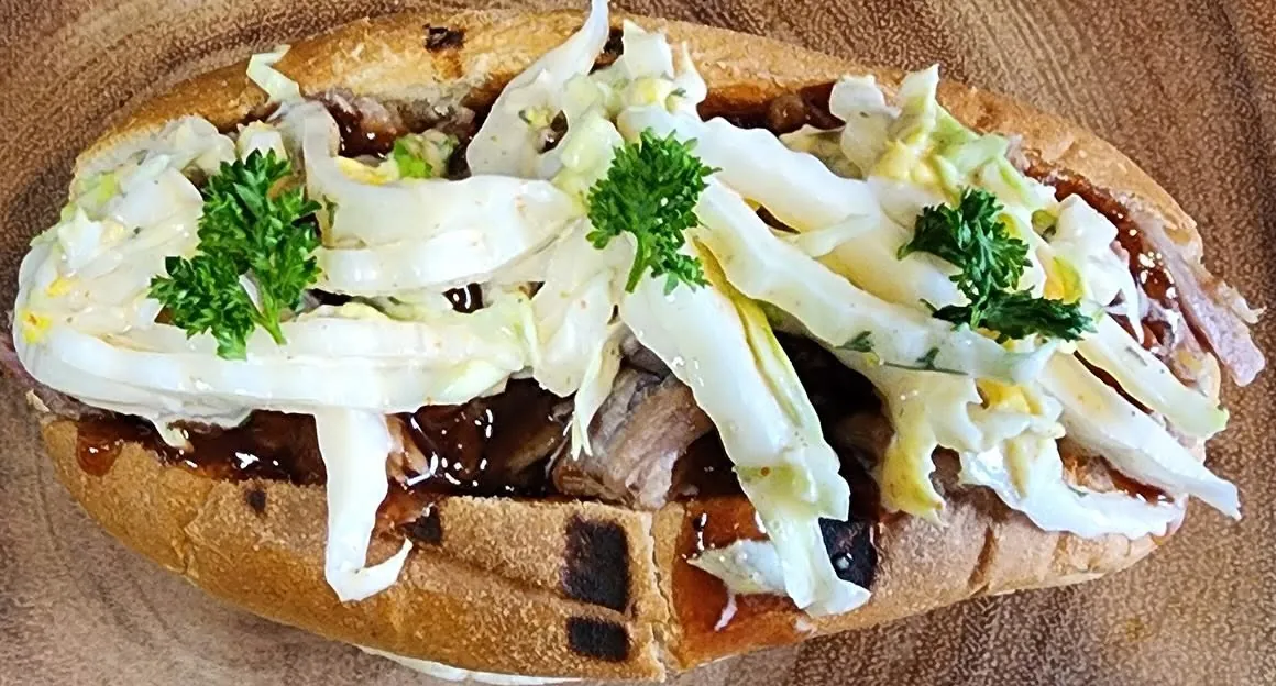 Close-up of a house-smoked pulled meat sandwich with coleslaw and fresh parsley from Global Fusion RVA