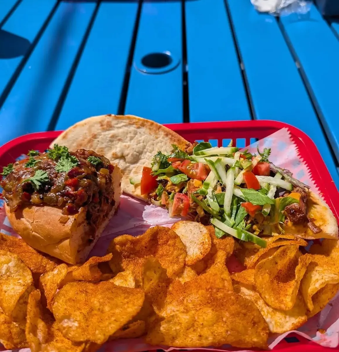 A pulled meat sandwich and a fresh vegetable wrap served in baskets with chips